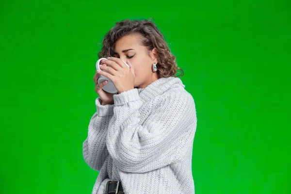 Sweet curly girl drinking hot cocoa standing against green background. — 스톡 사진