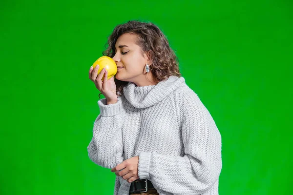 Afro-american girl smelling a big bite of ripe autumn apple, standing on green background. Vitamin food for healthy growth. — 스톡 사진