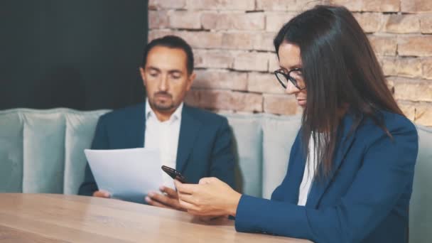 Dos empresarios trabajan en un café. El hombre está aprendiendo atentamente los documentos. La mujer se desplaza. De cerca. Copiar espacio . — Vídeos de Stock