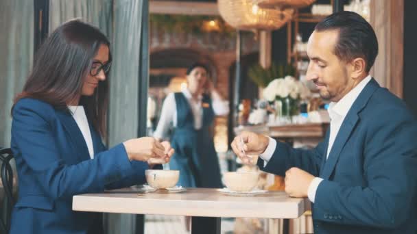 Two business people have business lunch. The woman and the man in a restaurant or a coffee shop are stirring and drinking coffee. Copy space. — Stock Video