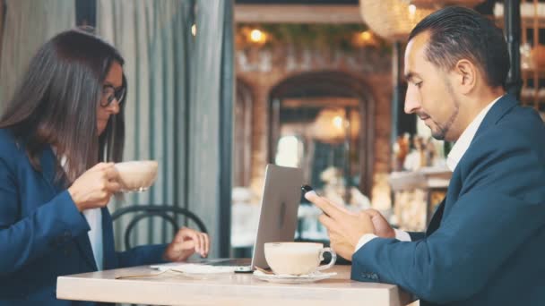 Deux hommes d'affaires déjeunent. La femme et l'homme dans un restaurant ou un café remuent et boivent du café. Ils travaillent avec téléphone et ordinateur portable. Espace de copie . — Video