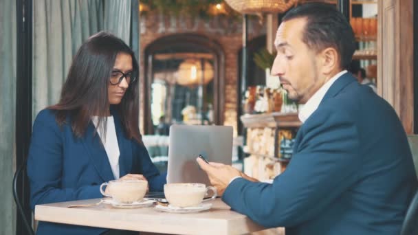 Twee zakenmensen lunchen samen. De man in een restaurant of koffieshop drinkt koffie en de vrouw werkt op een laptop. Kopieerruimte. — Stockvideo