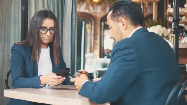 深い青色のスーツを着た2人のビジネスマンが働いている。男はタブレットに取り組んでいる。女性は買い物カードの助けを借りてインターネットで購入しています。閉めろスペースのコピー. — ストック動画