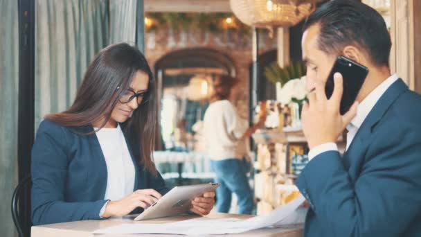 Two businesspeople in deep blue suits are working. Woman is using a tablet, sitting in coffee shop. Man is speaking on the phone. Close up. Copy space. — Stock Video