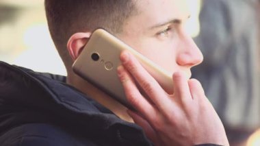 Handsome, attractive young man is on the phone, sitting on the bench. Copy space. Action. Animation. 4K.