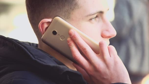 Um jovem bonito e atraente está ao telefone, sentado no banco. Espaço para cópia. Acção. Animação. 4K . — Vídeo de Stock