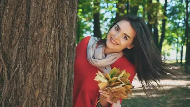 Happy smiling caucasian girl is showing up with a bunch of autumn leaves from tree caudex, isolated, on blurred park background. Close up. Copy space. — 비디오