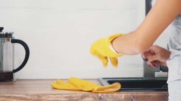女性はキッチンシンクとモダンなケトルの近くに黄色のゴム手袋を着用しています。作物だ閉めろ4k. — ストック動画