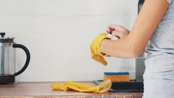 A mulher está colocando luvas de borracha amarela perto da pia da cozinha e chaleira moderna. Cultivo. Fecha. 4K . — Vídeo de Stock