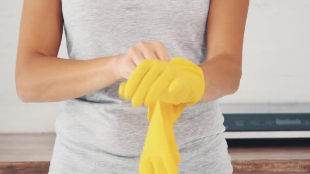 De vrouw trekt gele rubberen handschoenen aan in de buurt van een elektrisch fornuis. Gewas. Sluit maar af. 4k. — Stockvideo