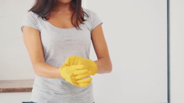 A mulher está colocando luvas de borracha amarela perto do fogão elétrico da cozinha. Cultivo. Fecha. 4K . — Vídeo de Stock