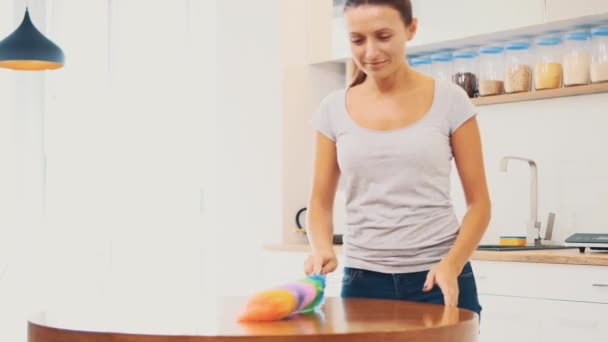 Una mujer con una camiseta gris apretada con un escote profundo limpia una gran mesa de cocina con un limpiador de polvo. De cerca. 4K . — Vídeo de stock