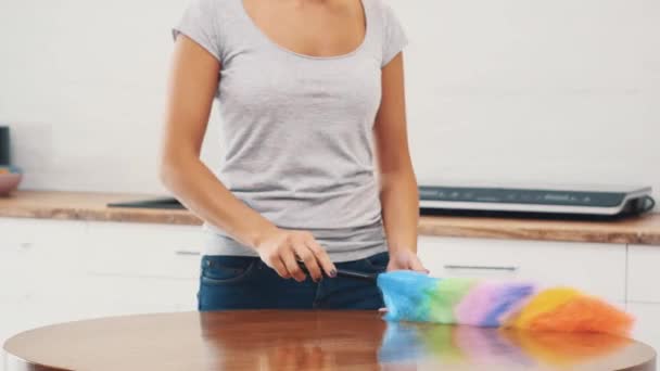 Een vrouw in een strak grijs T-shirt met een diepe halslijn veegt een grote keukentafel af met een stofzuiger. Gewas. Sluit maar af. 4k. — Stockvideo