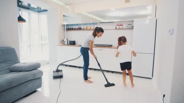 Mujer con su hija están aspirando el suelo de la cocina con baldosas blancas sin cepillo, solo tubería de aspiradora. Copiar espacio. 4K . — Vídeo de stock