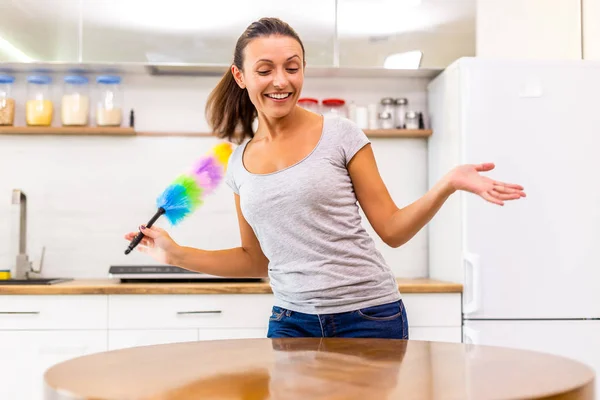 Energiegeladene Frau mit Regenbogenstaubwedel zu Hause, die das Ergebnis ihrer Arbeit genießt, weil jetzt alles leuchtet. — Stockfoto