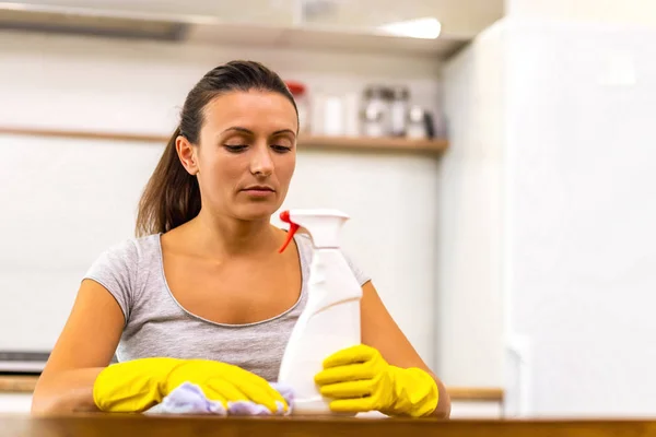 Lovely caucasian lady is bored of cleaning day after day and she sits at the table, with rag and spray on it, looking depressed. — Stock Photo, Image