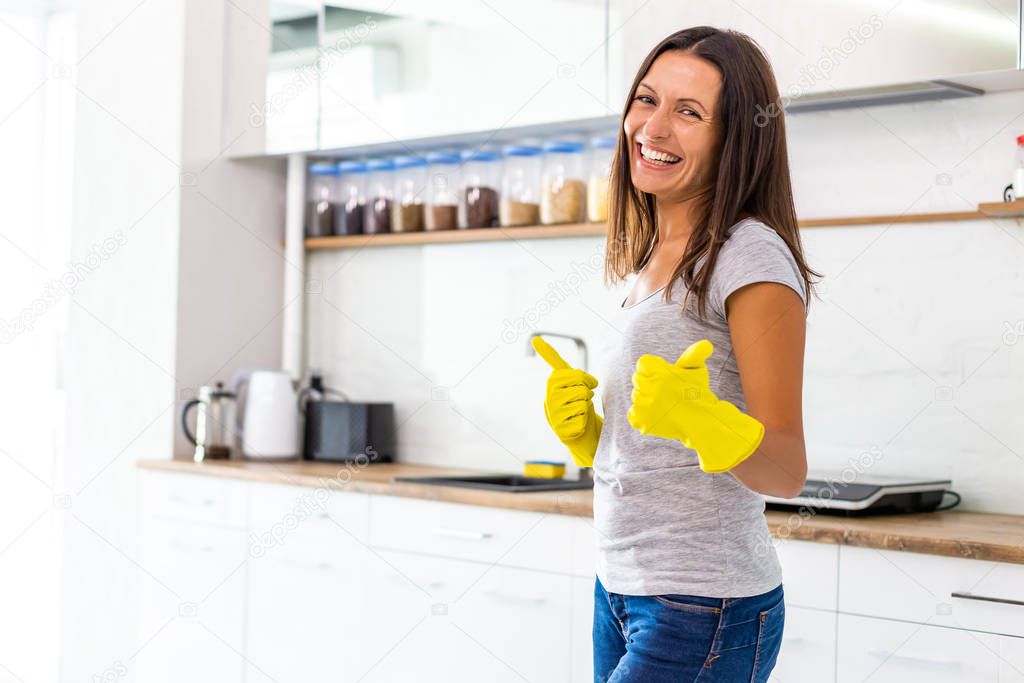 Determined wife in yellow gloves is ready and eager to start cleaning her modern kitchen and gives thumbs up.