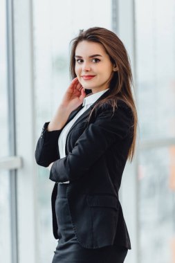 Neşeli kadın pencereden bakıyor, yeni ofisinde hoş duygular ve kendine güvenini ifade ediyor..