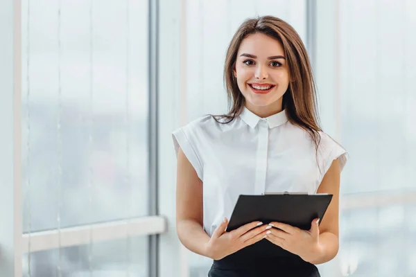 Positive smiling female teacher inspired with education ideas, stands holding paperholder in hands. — Stock Photo, Image