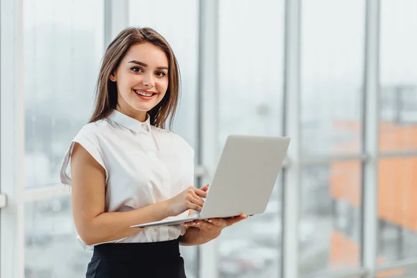 Радостная деловая женщина стоит в офисе, держа в руках ноутбук . — стоковое фото