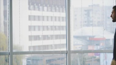 Resmi süitteki iş adamı şehir manzaralı panoramik pencerenin önünde duruyor. Ekin. Kapatın. Animasyon. 4K.