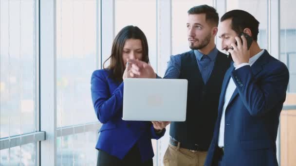 Pracownicy biznesowi rozmawiają o problemach, patrzą na laptopa. Jeden z nich rozmawia przez telefon. Odbiór. Zamazane tło. Zamknij drzwi. 4k. — Wideo stockowe