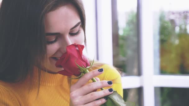 Hermosa chica morena está oliendo una rosa en un café. De cerca. Copiar espacio. 4K . — Vídeos de Stock