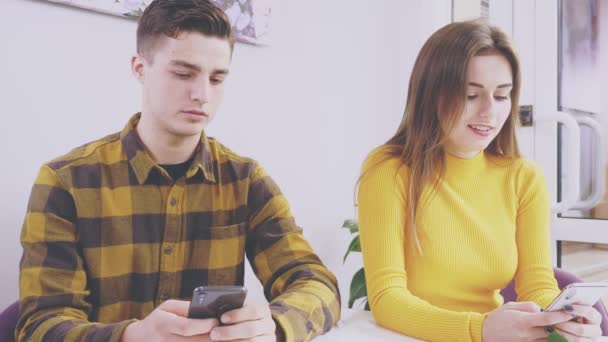 Adorable pareja está sentada en la mesa en la cafetería. Están filmando nuevas transmisiones en sus teléfonos celulares. De cerca. Copiar espacio. 4K . — Vídeo de stock