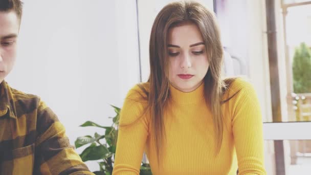 Adorable fille est assise à la table dans un café. Ils se montrent quelque chose sur le portable. Ferme là. Espace de copie . — Video