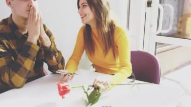 Adorable girl is sitting at the table in cafe. She is communicating with her boyfriend and showing him something on the cell phone. Sincere smile. Close up. Copy space.