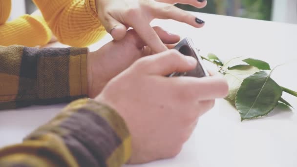 Entzückendes Mädchen sitzt am Tisch im Café. Sie kommuniziert mit ihrem Freund, der ihr etwas auf dem Handy zeigt. Nahaufnahme. Kopierraum. — Stockvideo