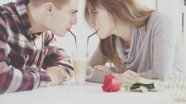 Couple of young people are in the cafe. The guy and the girl are drinking latte from one glass. Close up. Copy space. Action. Animation. 4K.