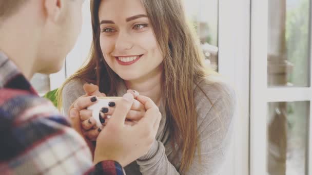 Una encantadora pareja sonriente está sentada en el café. Están sosteniendo una taza de café caliente. Vista de cerca. Copiar espacio. Acción. Animación. 4K . — Vídeos de Stock