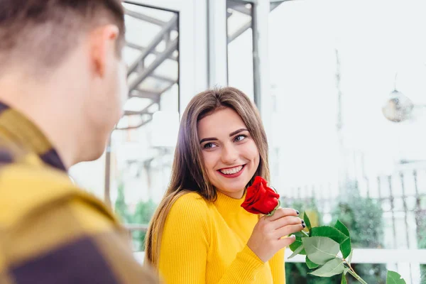 Namorado tem encontro com a namorada, dá-lhe uma grande rosa vermelha, ele sabe que as mulheres gostam de flores. Foco está na senhora irradiando com prazer, segurando uma flor . — Fotografia de Stock