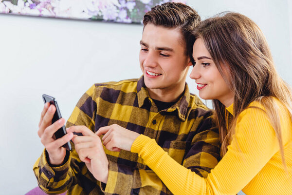 Lively young couple looking through photos on smartphone, smiling with pleasure as they relax at home.
