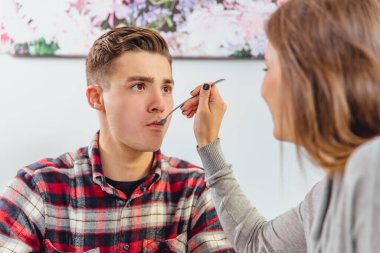 Beautiful couple in love is sitting in cafe, young woman is feeding her man, he looks a little bit puzzled.