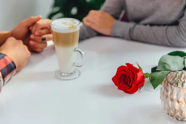 Cropped shot of woman in a grey sweater, holding her loved person hand, sitting at the table with latte and rose. — 스톡 사진