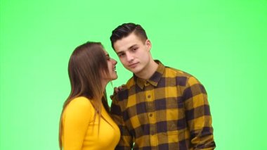 Woman is whispering a secret to her surprised young man on green background. Close up. Copy space. 4K.