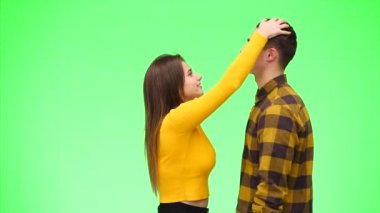 Meraklı kız, erkek arkadaşının saçlarını okşar ve yeşil bir arka planda onu öpmeye daha da yaklaştırır. Kapatın. Uzayı kopyala 4k.