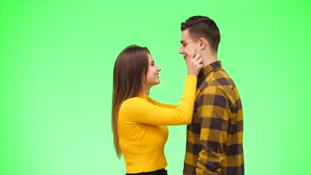 好奇心旺盛な女の子は、緑の背景に彼女のボーイフレンドの頬と耳を引っ張っています。鼻が擦れてる閉めろコピースペース4k. — ストック動画