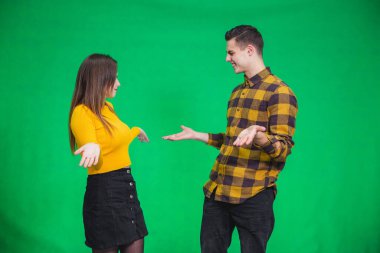 Young siblings dressed alike in yellow and black, looking at one another confused, throwing their hands.