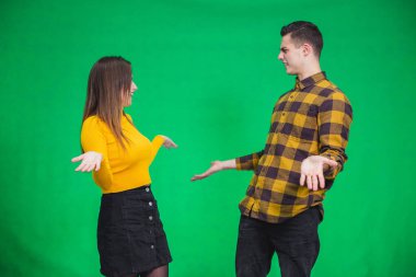 Young siblings dressed alike in yellow and black, looking at one another confused, throwing their hands.