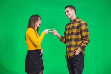 Funny caucasian man and woman, smiling and pointing with index fingers at one another while jokingly asking to change clothes because they looks alike.