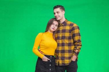 Inspired young people looking ahead, dreaming about their future together, while standing on green background, embracing.