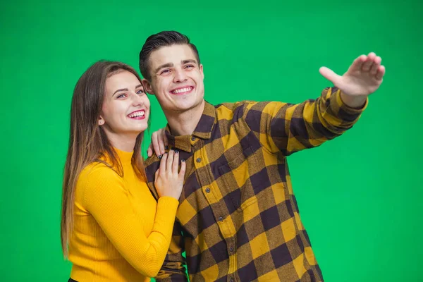 Portrait of happy couple looking and pointing into the distance, isolated on green background. — Stockfoto