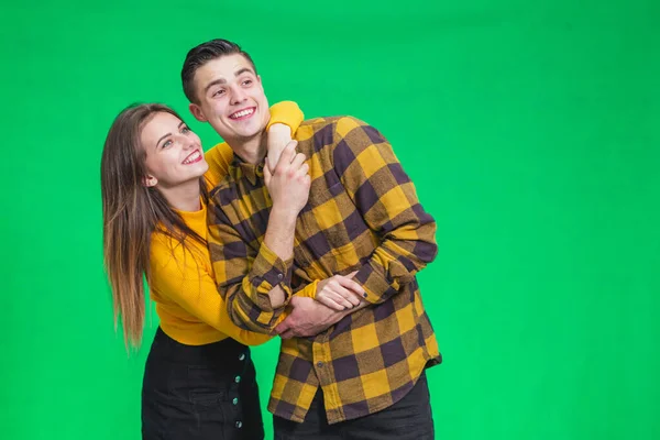 Portrait of a cheerful young couple standing isolated over green background, looking far away, smiling. — Stockfoto