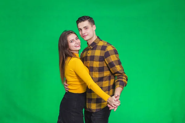 Sweet couple dressed in yellow, dancing slow ballroom dance over green background, during their leisure time.