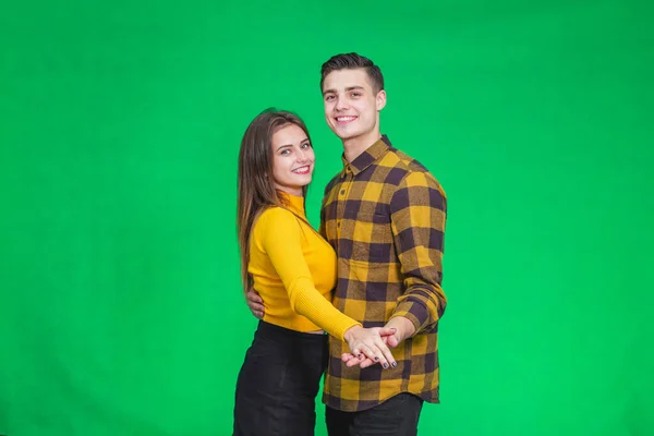 Sweet couple dressed in yellow, dancing slow ballroom dance over green background, during their leisure time.