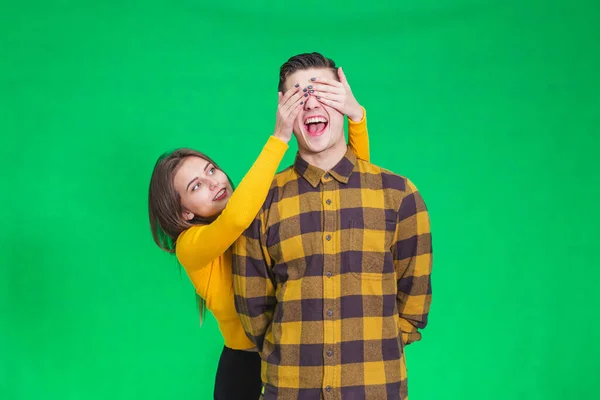 Playful girl covering boyfriends eyes with hands on green background. — Stockfoto