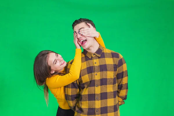 Verspieltes Mädchen, das die Augen seiner Freunde mit den Händen auf grünem Hintergrund bedeckt. — Stockfoto